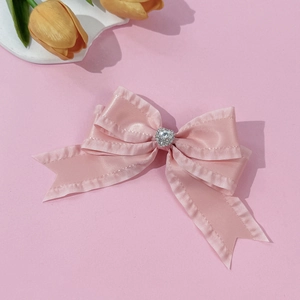 Détail d'une pince à cheveux en satin rose avec strass en cœur et bords à volants élégants