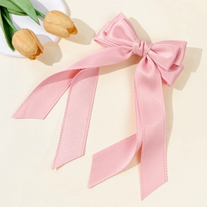 Detail of pink satin bow hair clip with long ribbons on a soft beige background