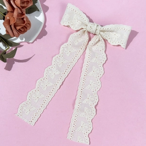 Detail of off-white lace bow hair clip with intricate crochet patterns and long ribbons