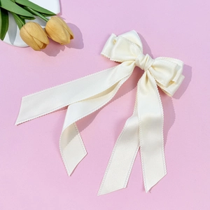 Close-up of elegant ivory satin ribbon hair clip with delicate wavy edges on pink surface