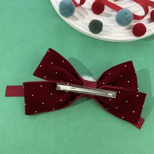 Elegant red velvet bow hair clip with rhinestones and white pom-pom on green background