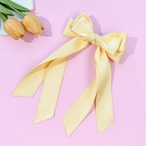 Detailed macro view of cream yellow satin ribbon bow hair clip with wavy edges