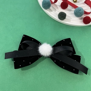Detail of black velvet bow hair clip with silver beads and a fluffy white pompom ball