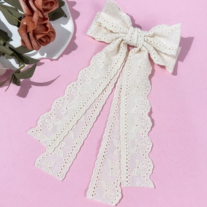 Close-up of white lace bow hair clip with floral embroidery and long ribbons