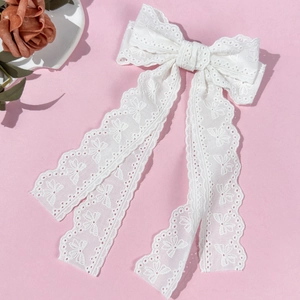 Detailed close-up of white lace bow hair clip with floral embroidery and long ribbons