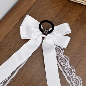 Elegant white satin bow hair tie with lace edges and handmade label on wood surface