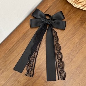 Elegant black satin bow hair tie with long lace ribbons on a vintage wooden surface
