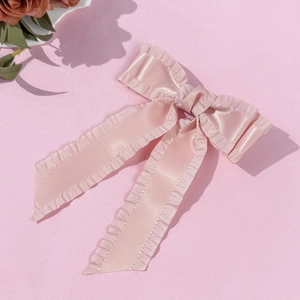 Détail de la pince à cheveux en satin rose avec bords plissés et ruban élégant