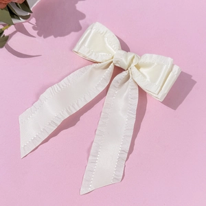 Gros plan d'une barrette à cheveux nœud crème en satin avec bords à volants et rubans