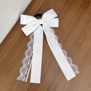 Detail of white satin bow hair tie with elegant lace embroidery on long ribbons