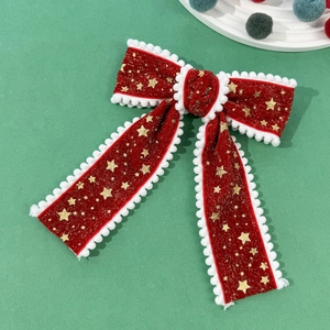 Detail der roten Samt-Haarschleife mit goldenen Sternen und weißen Pompons für Weihnachten