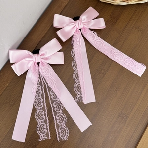 Detail view of two pink satin hair scrunchies with elegant lace trim on dark wood