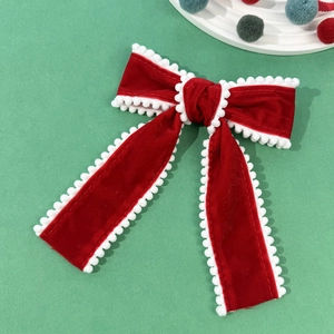 Detail einer roten Samt-Schleife mit weißen Pom-Poms auf einem festlichen grünen Hintergrund