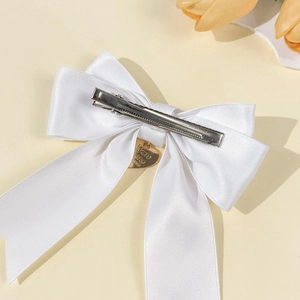 Detail einer eleganten weißen Satinschleife mit goldenem Herzanhänger und Metall-Haarspange