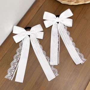 Detail view of white satin bow hair ties with lace trim on a dark wooden surface
