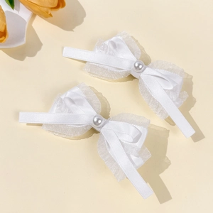 Détail des barrettes nœuds en satin blanc avec bordure dentelle et perle centrale