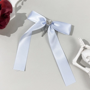 Close-up of light blue satin bow hair clip featuring heart rhinestone and cross pendant