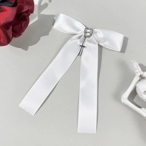 Detail of white satin bow hair clip with heart rhinestone and metal cross pendant