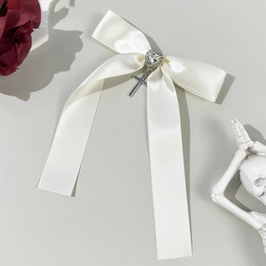 Detail view of a creamy white satin bow hairclip with heart gemstone and silver cross pendant