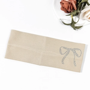 Beige knitted ribbed headband with sparkling rhinestone bow detail on white background