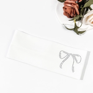 Detail of white ribbed headband with sparkling rhinestone bow on a soft fabric texture