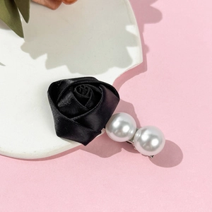Détail de la pince à cheveux rose en soie noire avec perles blanches sur plateau