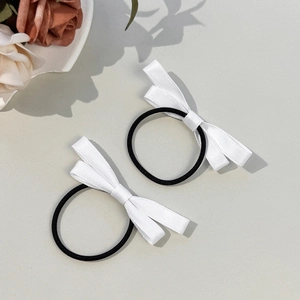 Gros plan d'élastiques à cheveux avec nœuds en satin blanc sur un fond gris minimaliste