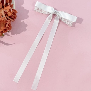 Détail de la pince à cheveux en dentelle et ruban blanc avec une perle au centre