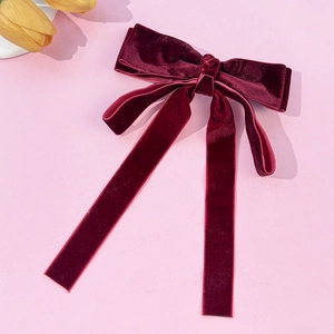 Close-up of burgundy velvet bow hair clip with long ribbons on pink background