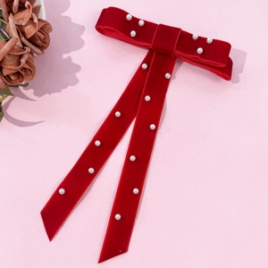 Close-up of red velvet bow hair clip with white pearls and long ribbon on pink backdrop