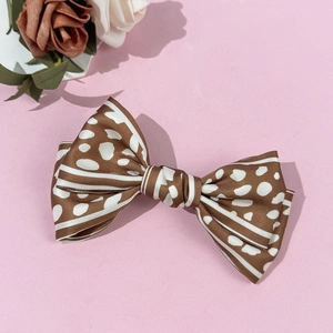 Elegant brown satin leopard bow hair clip with white polka dots on soft pink background