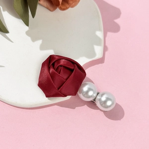 Détail de la pince à cheveux rose en soie bordeaux avec perles blanches sur fond rose