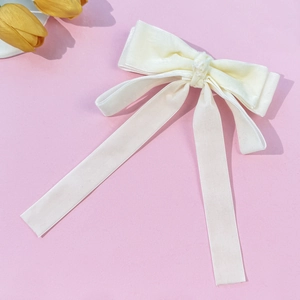 Close-up of elegant cream velvet bow hair clip with long ribbons on pink background