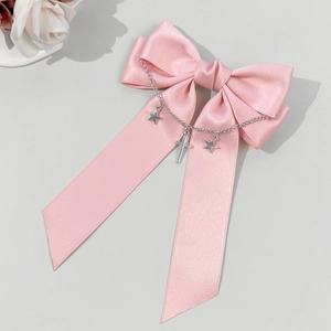 Détail d'une pince à cheveux nœud en satin rose avec chaînette étoile et croix