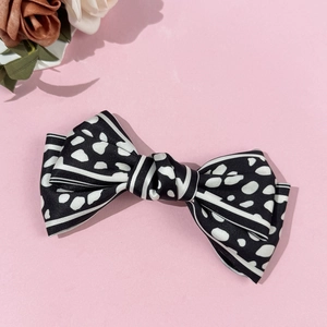 Detailed view of a retro polka dot and striped satin bow hair clip on a pink backdrop