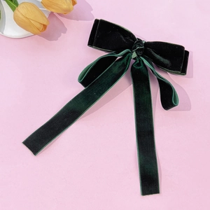 Close-up of elegant dark green velvet bow hair clip with long streamers on pink background