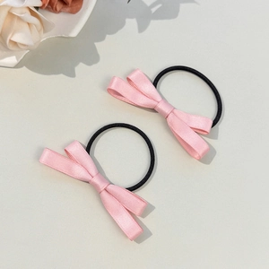 Détail de chouchous à nœuds en satin rose avec élastiques noirs sur fond beige doux