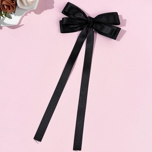 Elegant black satin bow hair clip with long ribbons on a pink background with flowers