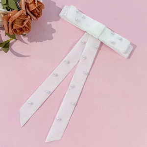 Close-up of white velvet bow hair clip with elegant pearl beads and long ribbon streamers