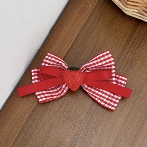 Red gingham bow hair clip featuring a cute strawberry resin charm on a wooden surface