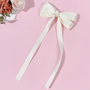Close-up of cream white satin bow hair clip with long ribbons on pink background