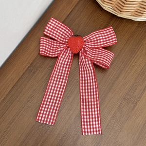 Detail of red gingham bow hair clip with cute 3D strawberry charm on wooden background