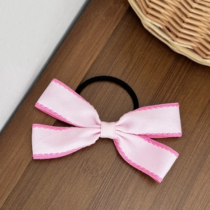 Dettaglio dell'elastico per capelli con fiocco rosa e cuciture su piano in legno