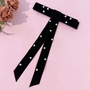 Detail of black velvet bow hair clip with white pearls and long ribbons on pink backdrop