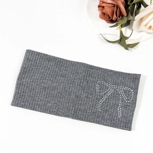 Detail of grey ribbed knit headband featuring a sparkling rhinestone bow on white background