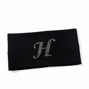 Macro detail of black knitted yoga headband featuring a sparkling rhinestone H initial
