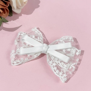 Detail of white lace bow hair clip showing delicate embroidery and satin ribbon layers
