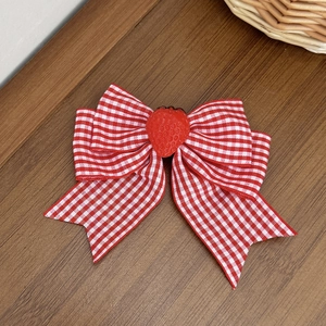 Detail of red gingham bow hair clip with a cute strawberry charm on wooden texture