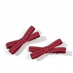 Dettaglio di due fermagli per capelli a fiocco rosso scuro con bordi bianchi e clip in metallo