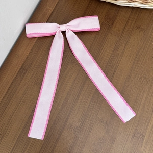 Fiocco per capelli rosa con bordi ondulati e nastri lunghi su sfondo in legno